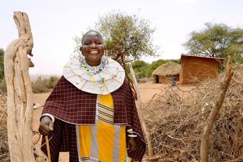 Mama Neema stands at the entrance of her traditional boma (homestead) where she built three houses for her family in Kimokouwa village in Arusha, Tanzania UN WOMEN